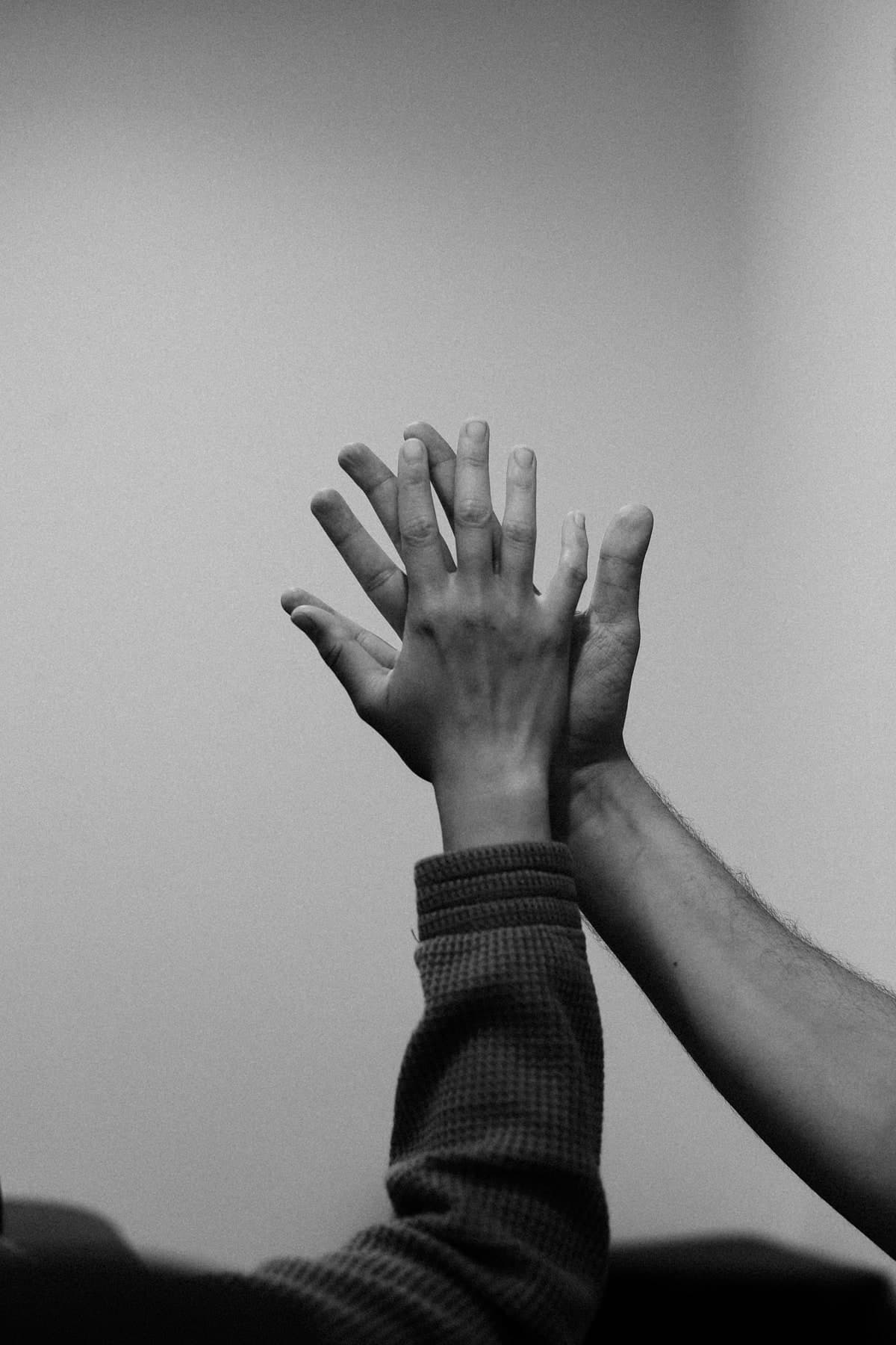 Black and white photo of two raised hands high-fiving against a plain grey background, one a child's hand in a knit sleeve and one an adult's hand