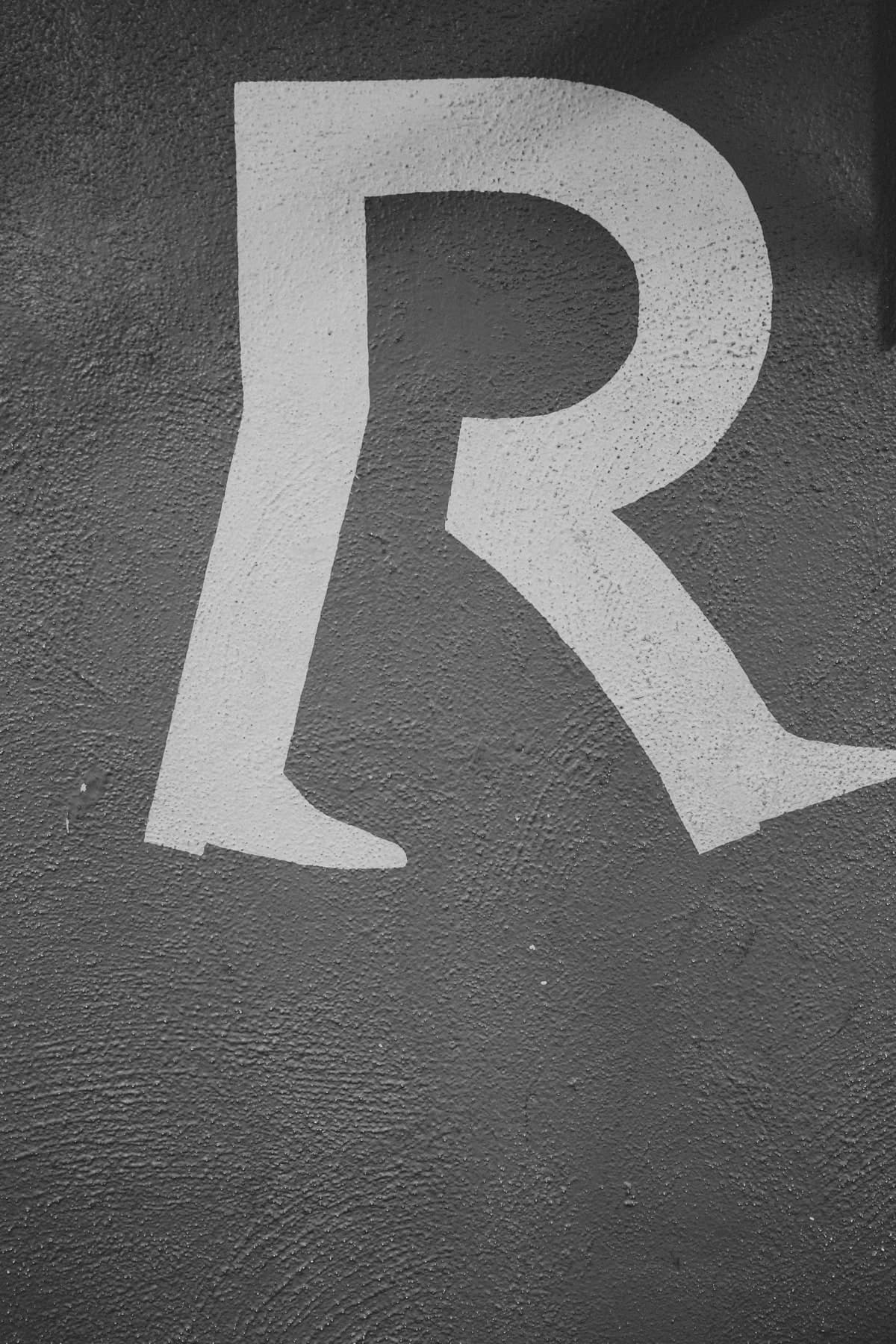 Large white painted letter R on a textured grey wall, black and white photograph