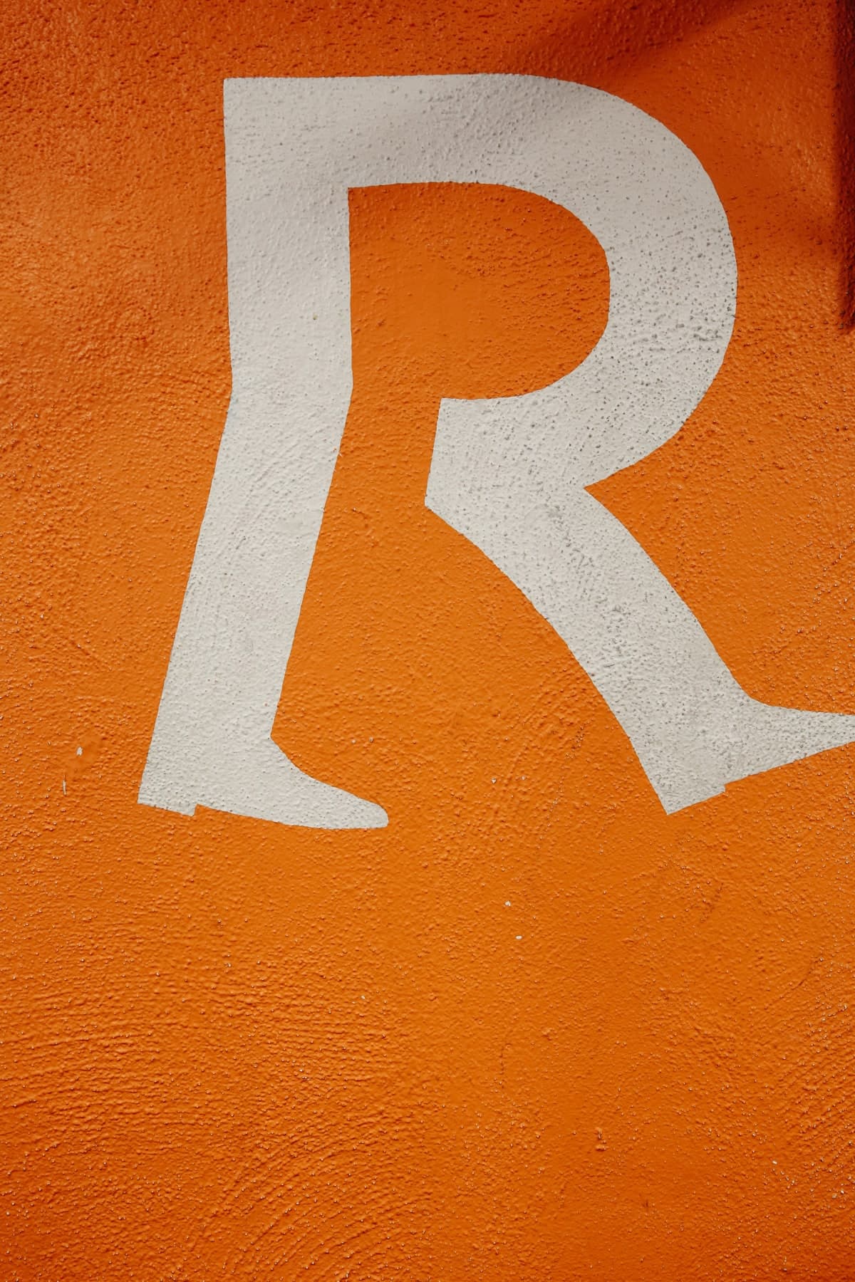 Large white painted letter R on an orange textured wall